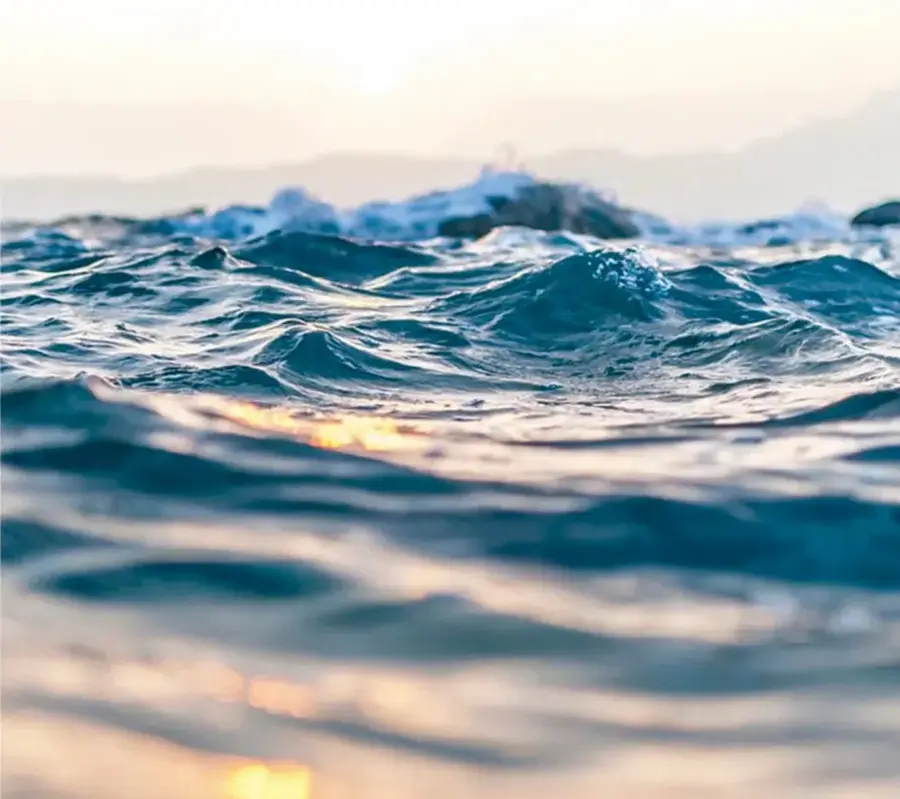 Fotografía de olas del mar azul con luz del sol asomando en el horizonte, captando el reflejo dorado sobre el agua.