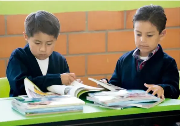 Dos niños sentados frente a una mesa revisando libros y cuadernos.