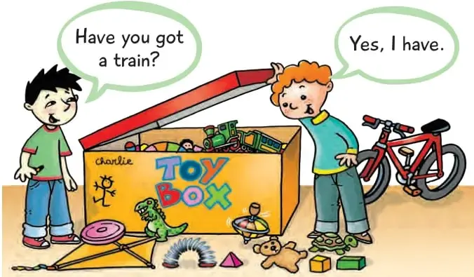 Niño junto a una caja de juguetes amarilla con la palabra 'Toy Box'; otro niño saca un tren rojo. Al fondo, una bicicleta roja.