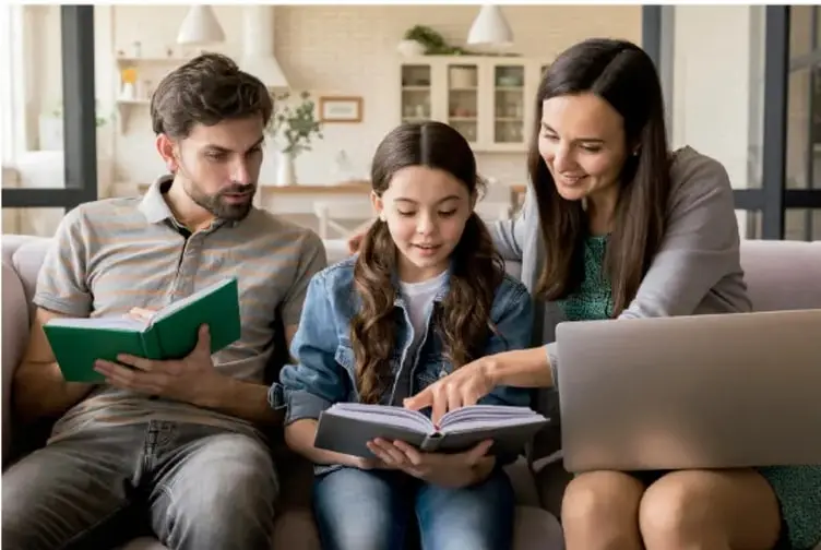 Familia sentada en un sillón: el padre lee un libro verde, la madre señala una laptop y la hija sostiene un cuaderno.