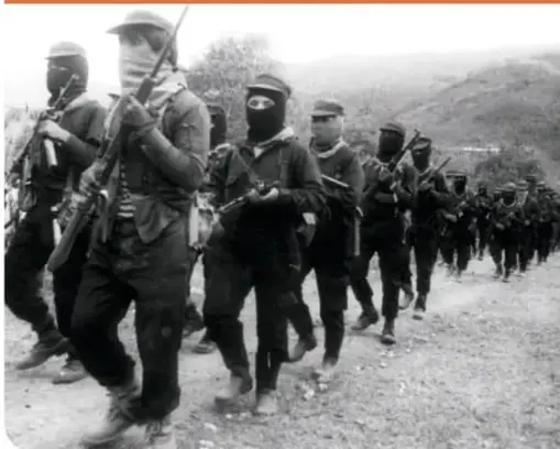 Columna de zapatistas. Grupo de personas encapuchadas y armadas marchando en una carretera.