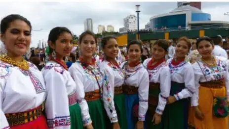 Fotografía de un grupo de niñas vestidas con trajes típicos de colores vivos (blusas blancas bordadas, faldas verdes y rojas) durante una presentación de danza folclórica en un espacio público.