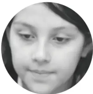 Fotografía en blanco y negro, recortada en círculo, del rostro de una niña con mirada pensativa y baja, que ilustra la reflexión sobre la migración.