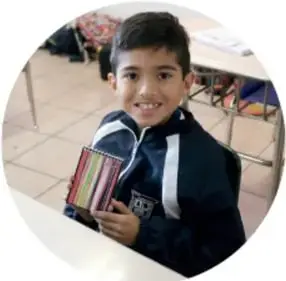 Niño de primaria sonriente sosteniendo un libro o cuaderno.