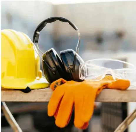 Equipo de protección personal: casco amarillo, careta de soldar, audífonos de protección y guantes naranjas sobre una mesa de trabajo