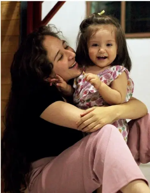 Madre o cuidadora abrazando y riendo con una niña pequeña; ilustra la conexión emocional y expresión positiva de sentimientos.