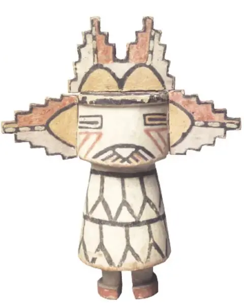 Figura tipo kachina de águila: cabeza rectangular con pintura geométrica en ocre y negro, alas en forma escalonada y cuerpo blanco con líneas negras verticales.