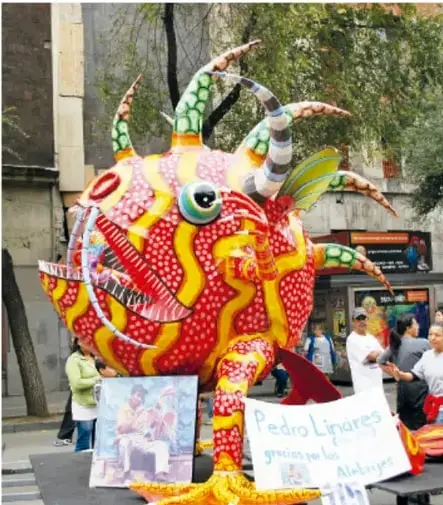 Alebrije gigante en forma de pez o criatura marina, exhibido en la calle con personas alrededor.