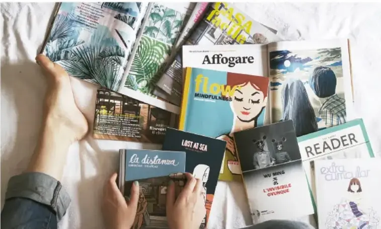 Fotografía de una cama o cobertor blanco con varias personas leyendo revistas y libros; se distinguen títulos como Affogare, flow Mindfulness, Lost at sea, La distancia, Reader y extra curricular.