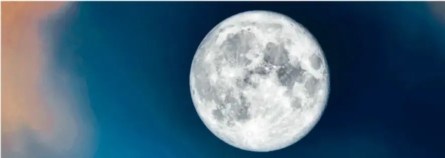 Fotografía de la Luna llena sobre cielo azul con nubes, ilustrando la fase de luna llena.