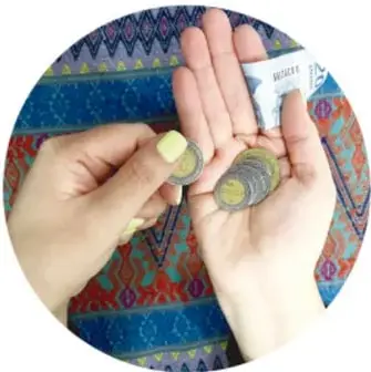 Fotografía circular de unas manos contando monedas y un billete sobre una tela colorida tejida.