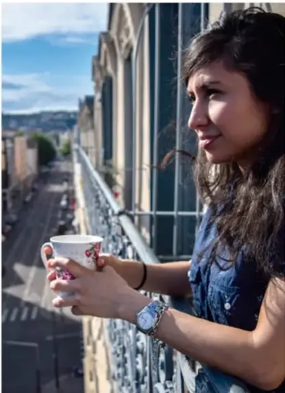 Fotografía de una joven de cabello oscuro sosteniendo una taza, apoyada en una barandilla con vista a una calle urbana; ilustra la presencia juvenil en espacios públicos y digitales.