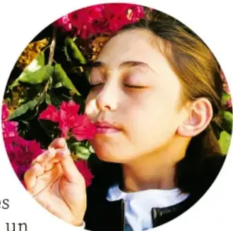 Fotografía de una niña con los ojos cerrados oliendo una flor rosada (bougainvillea), ilustrando el uso de los sentidos.