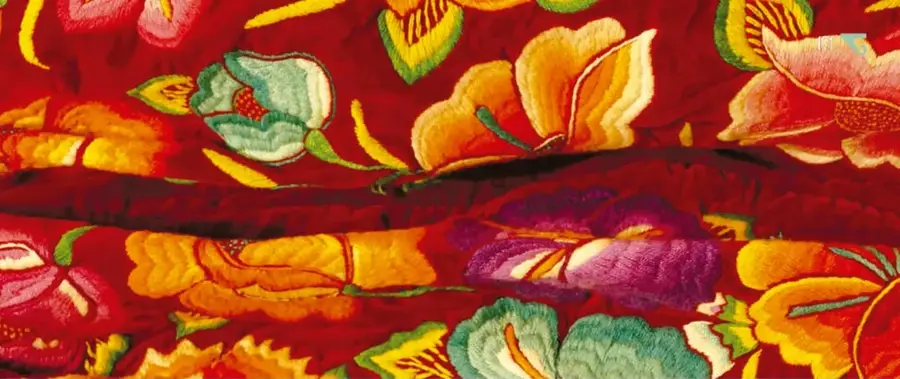 Tela bordada roja con flores grandes bordadas en naranja, amarillo, verde, rosa y morado.