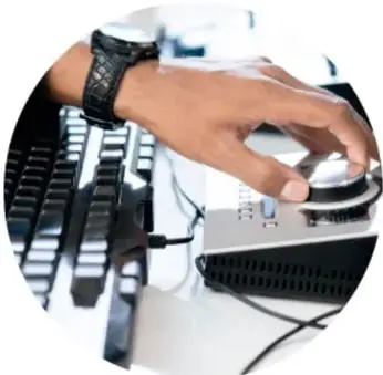 Fotografía circular de una mano con reloj manipulando un teclado y un aparato de audio: el trabajo del diseñador de sonido.
