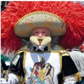 Persona disfrazada con gran penacho rojo y traje bordado, posiblemente un danzante o personaje de la fiesta comunitaria.