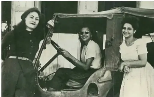 Fotografía histórica en blanco y negro de tres mujeres, presumiblemente las hermanas Mirabal, junto a un vehículo.