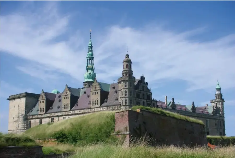 Fotografía del Castillo de Kronborg (Elsinor, Dinamarca), con torres verdes y murallas sobre una colina, bajo cielo azul con nubes.