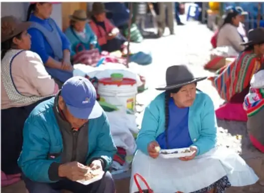 Fotografía de un mercado o tianguis al aire libre donde varias personas, en su mayoría mujeres con vestimenta tradicional, venden productos sentadas en el suelo.
