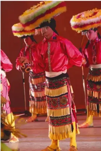 Bailadores con trajes tradicionales rojos, faldones con flecos y sombreros adornados, realizando una danza en grupo sobre un escenario.