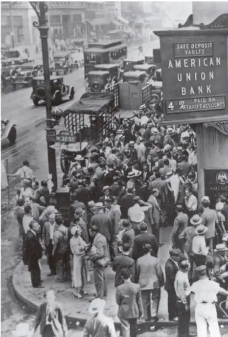 Fotografía en blanco y negro de una multitud frente al American Union Bank en Nueva York, durante la crisis de 1929. Se observa un letrero que dice 'SAFE DEPOSIT VAULTS' y '4% PAID ON THRIFT ACCOUNTS'.