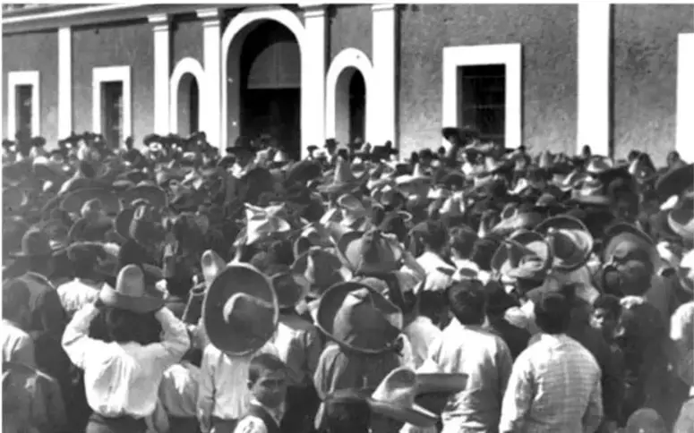 Fotografía en blanco y negro de una multitud reunida frente a un edificio con arcos, probablemente durante la Revolución Mexicana.
