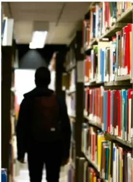 Fotografía de una persona caminando entre estantes llenos de libros en una biblioteca.