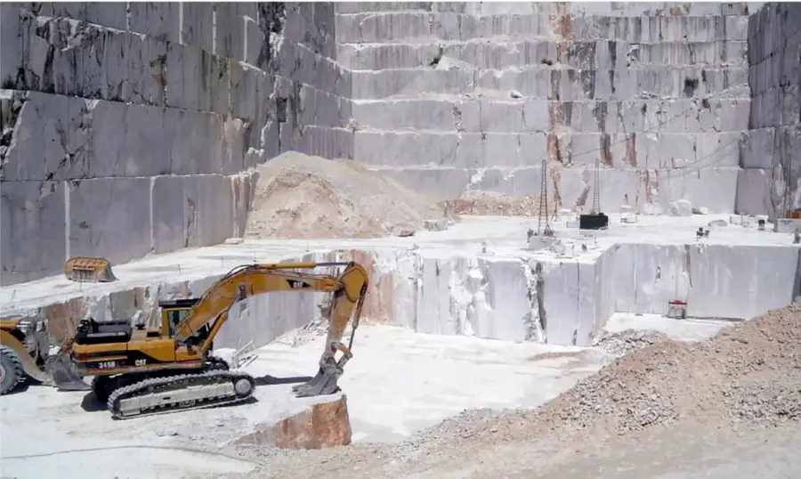 Cantera a cielo abierto con paredes de piedra blanca en escalones y una excavadora amarilla CAT trabajando.