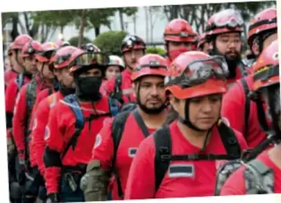 Fotografía de un grupo de voluntarios con uniforme rojo y cascos, integrantes de la Brigada de Rescate Topos Tlatelolco, formados y listos para una labor de rescate.