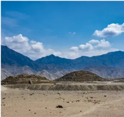 Fotografía de un paisaje árido con montañas y restos arqueológicos en el valle de Caral, Perú.