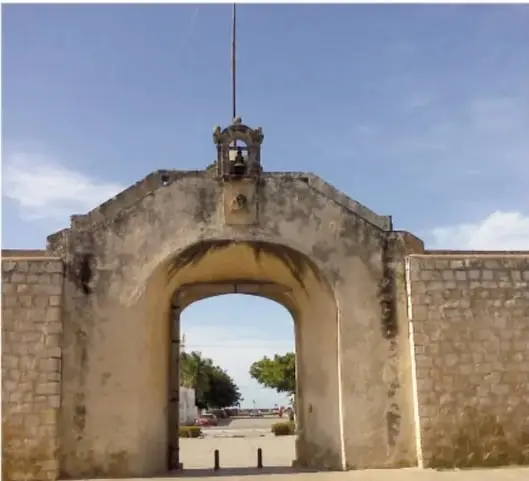 Fotografía de la Puerta de Tierra: arco de piedra con campana superior y mirador con skyline.