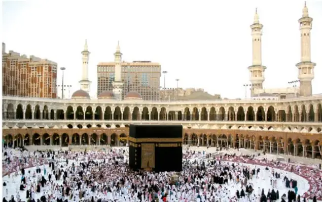 Fotografía aérea de la Gran Mezquita de La Meca durante una peregrinación: se observa la Kaaba, un gran cubo negro, rodeada por multitud de fieles, con minaretes y edificios alrededor.