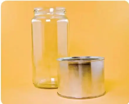 Fotografía sobre fondo amarillo con dos objetos: a la izquierda un frasco de vidrio transparente y alto, a la derecha una lata cilíndrica de metal opaco y plateado.