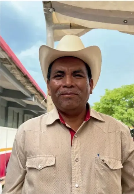 Fotografía de un hombre indígena adulto con sombrero de ala ancha, camisa clara, de pie en un espacio urbano o de mercado, ilustrando a un hablante de lengua originaria.