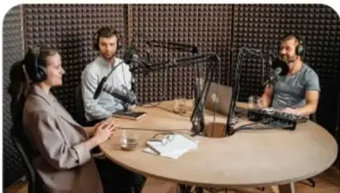 Tres personas con micrófonos y audífonos en un estudio de grabación (medio radiofónico).