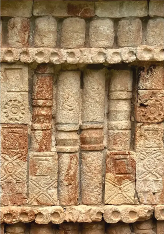 Fotografía de un muro de arquitectura prehispánica mexicana con columnas cilíndricas, relieves geométricos y rosetas talladas en piedra de tonos beige y ocres, posiblemente de la zona arqueológica de Malinalco o Monte Albán.