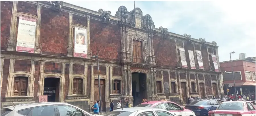 Fotografía actual de la fachada del Museo de la Ciudad de México: edificio colonial de dos pisos con muros de piedra rojiza, portada tallada, ventanales con marcos de piedra, carteles y personas en la banqueta, con autos y un camión en la calle.