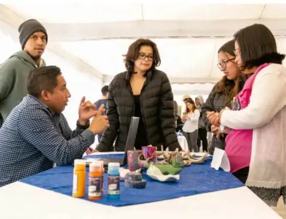 Fotografía de un grupo de personas reunidas alrededor de una mesa con muestra de materiales, conversando en una actividad comunitaria al aire libre.