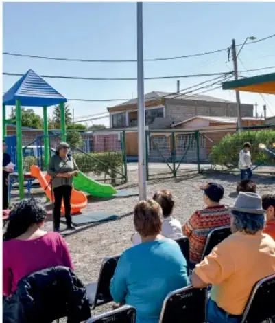 Fotografía de una asamblea o reunión comunitaria al aire libre en un parque; una persona está de pie dirigiéndose a un grupo de asistentes sentados en sillas.