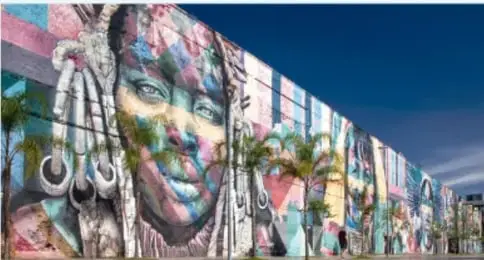 Mural de un pavo real azul y verde pintado sobre un muro curvo de color salmón.