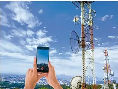 Fotografía de una persona sosteniendo un teléfono móvil frente a una antena de telecomunicaciones.