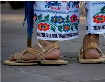 Fotografía de personas con calzado tradicional y faldas bordadas, representando vestimenta indígena.