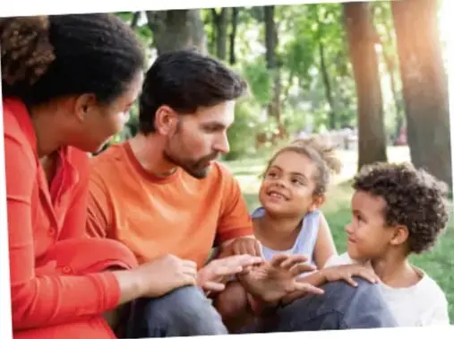 Fotografía de una familia (padre, madre y dos niñas) sentada en el pasto de un parque conversando juntos.