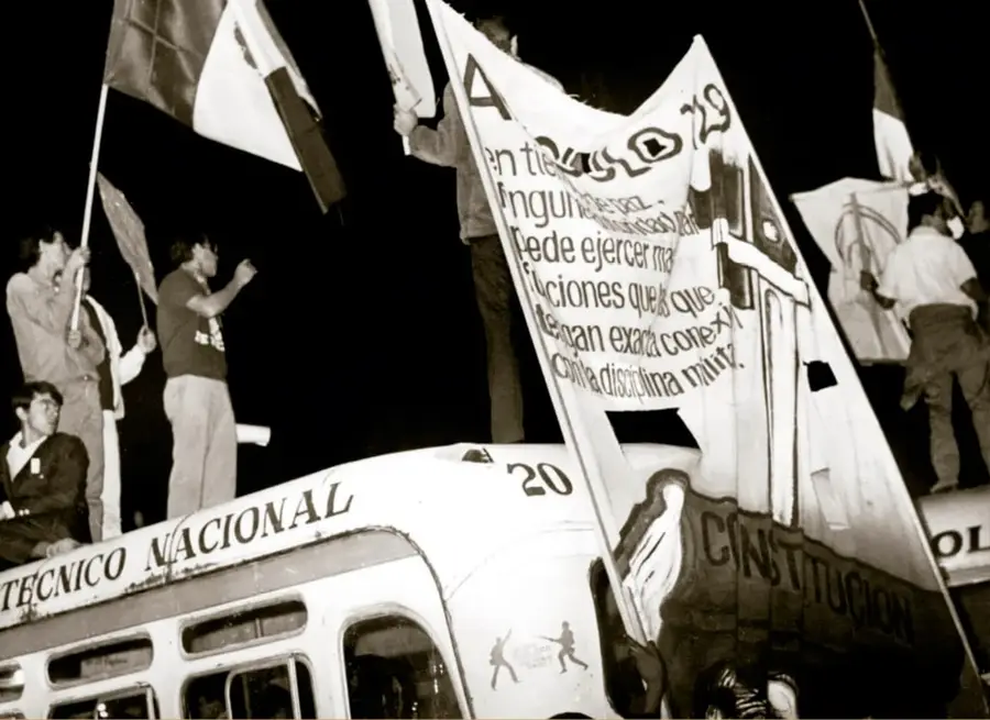 Fotografía histórica en blanco y negro: estudiantes del Instituto Politécnico Nacional en un mitin cerca del Zócalo de la Ciudad de México, agosto de 1968. Se observan jóvenes de pie sobre autobuses, portando banderas y enormes mantas con consignas escritas a mano (una manta menciona 'La Constitución' y otra habla de ejercer funciones); una unidad de transporte rotulada 'TÉCNICO NACIONAL' domina la escena.