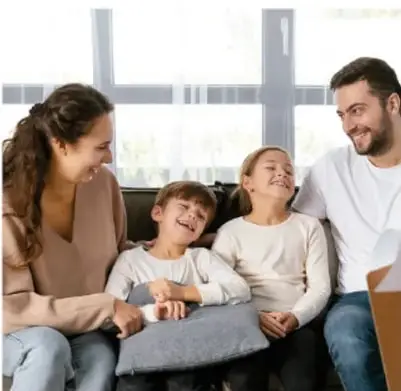 Fotografía de una familia (padre, madre y dos hijos) sentada en un sillón, conversando y sonriendo en un ambiente cálido de hogar, ilustrando el diálogo familiar propuesto en la sección 'Situaciones para aprender en familia'.