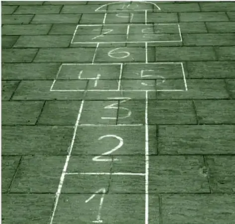Fotografía en tono verde del juego de ¿Saltas? dibujado con gis en el piso: líneas numeradas del 1 al 6 dispuestas como marcas de brinco (con dos casillas en pares en la parte alta).
