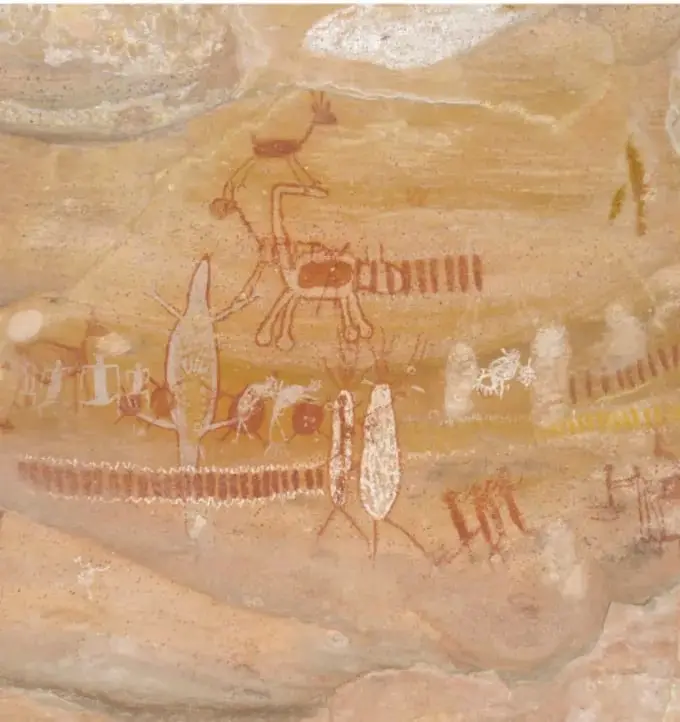 Fotografía de un panel rupestre de la sierra de Capivara (Brasil): muchas figuras humanas estilizadas en rojo y blanco, árboles, animales y hileras de puntitos que sugieren una ceremonia colectiva.