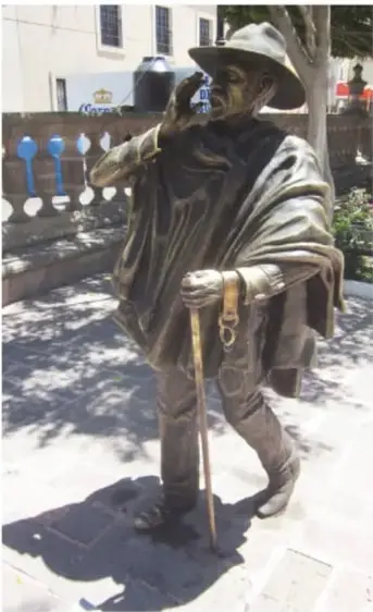 Estatua de bronce de la vendedora de flores: mujer con vestido y canasta llena de flores moradas, junto a un jarrón de piedra.