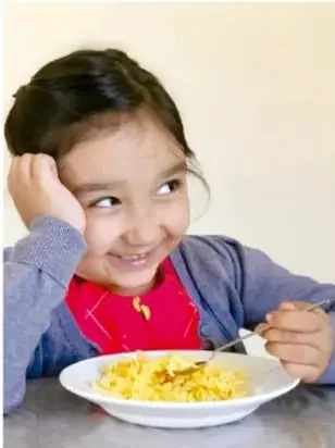 Niña comiendo cereal con leche de un plato blanco, con una cuchara.