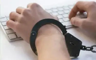 Manos escribiendo en un teclado con un brazo encadenado, representando la ciberadicción.